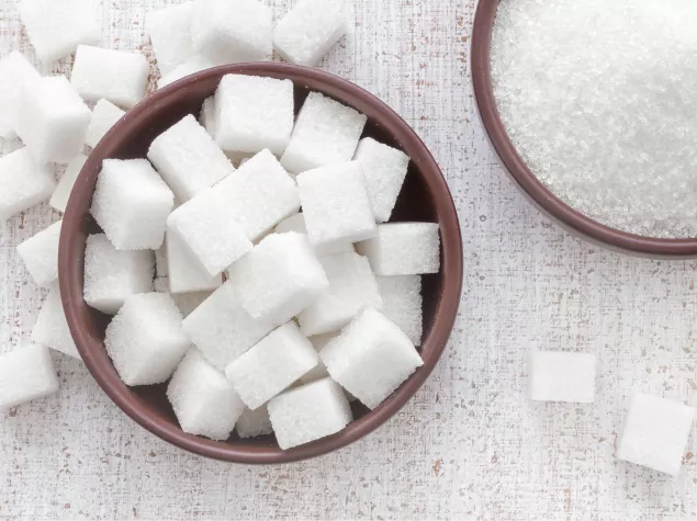 A bowl of white granulated sugar and a bowl of white sugar cubes