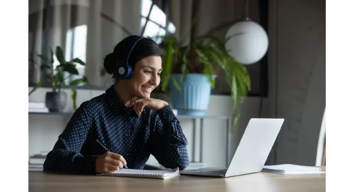 A happy Indian lady sitting at a lap top learning and taking notes